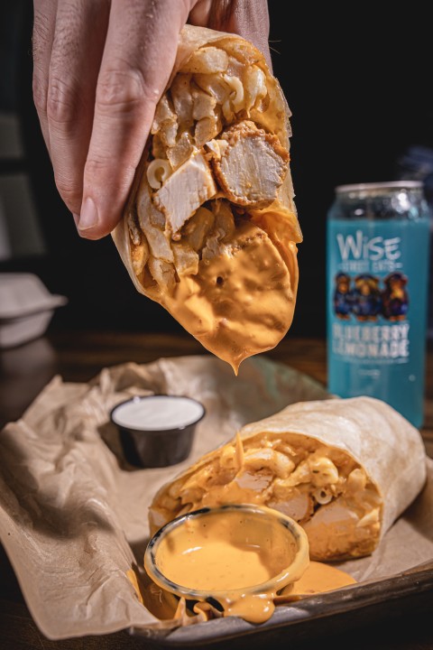A glazed chicken wing lifted from a basket of wings and ranch