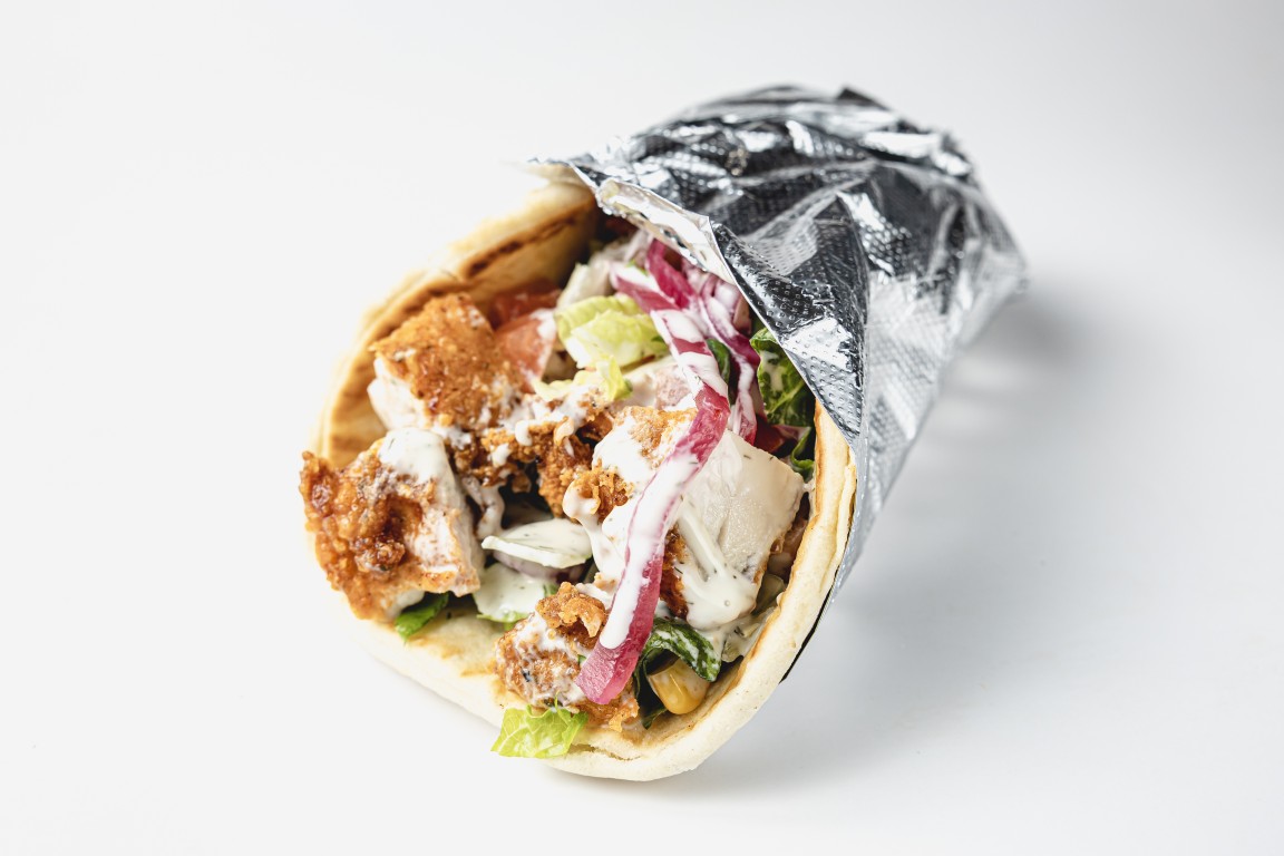 Gyro wrap in pita with chicken, salad, pickled onions and sauce, half wrapped in foil