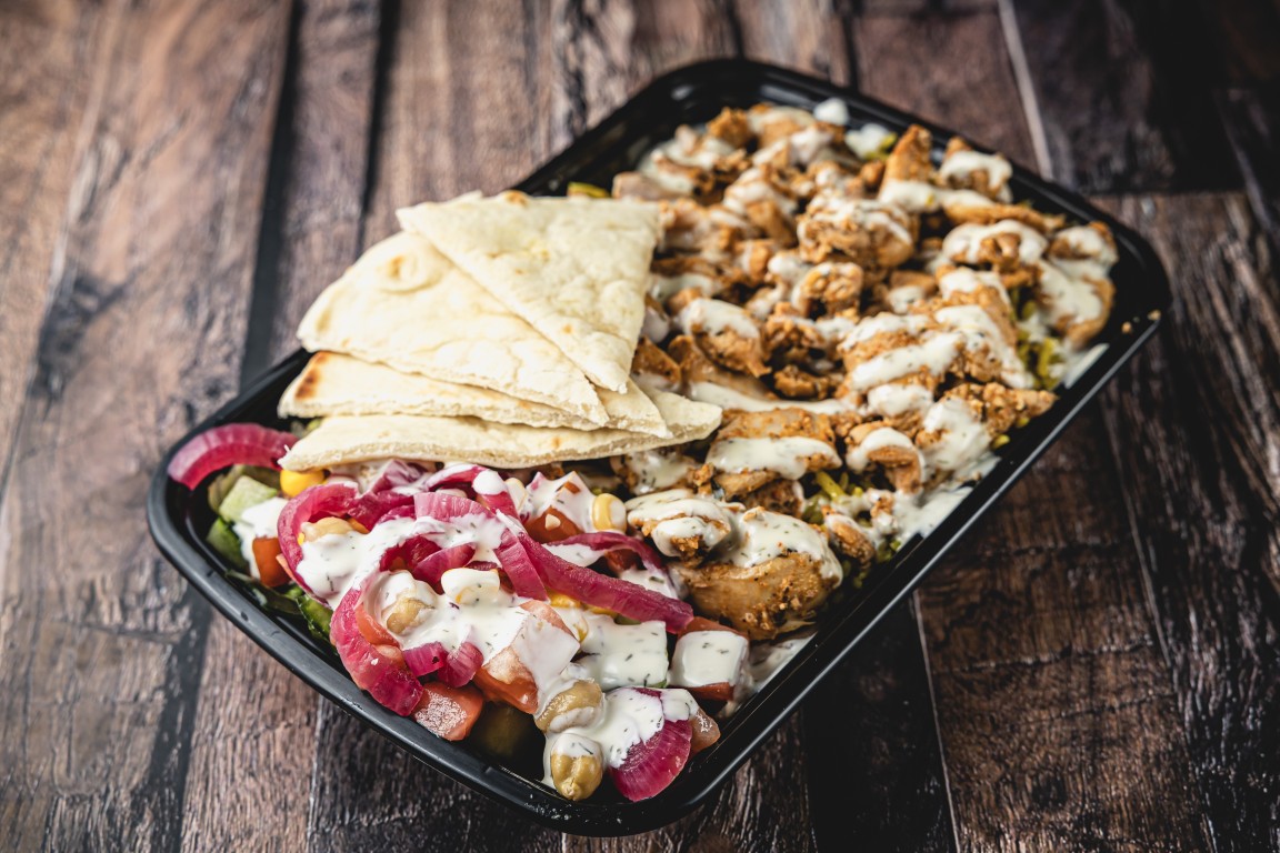 Rice bowl with chicken, salad, pickled onions and pita slices in a takeaway tray